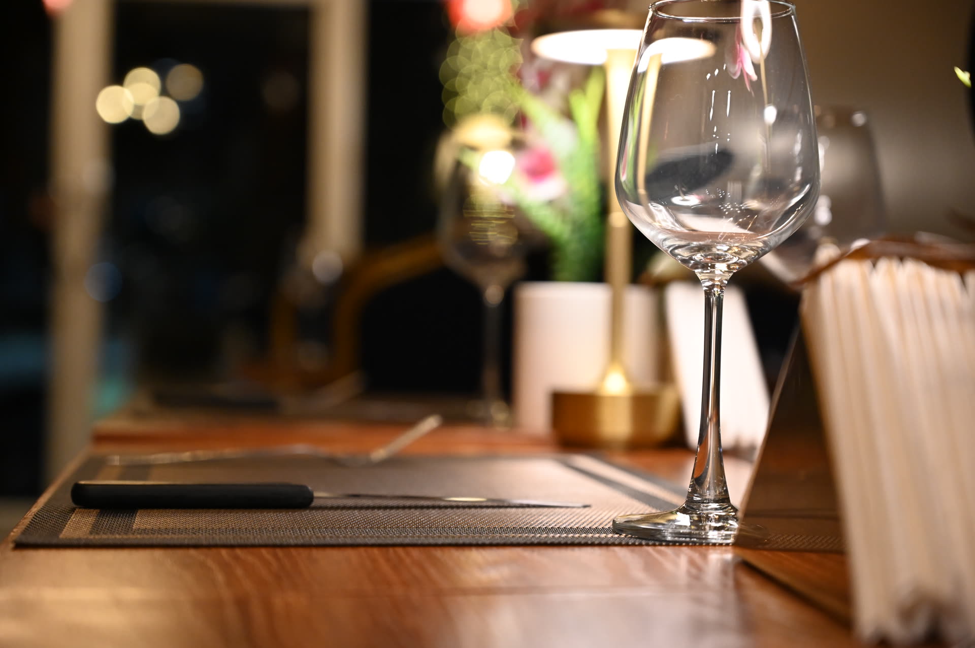 Glass of red wine glowing in warm light, on a table in a dimly lit dining room