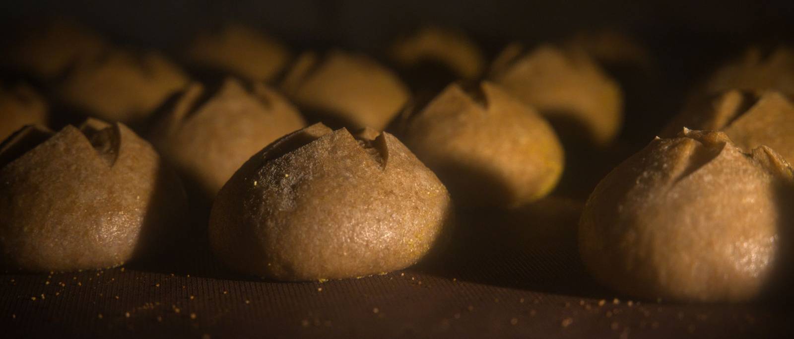 Pâini rotunde crestate în cruce, crescând în cuptor, în lumina caldă a vetrei
