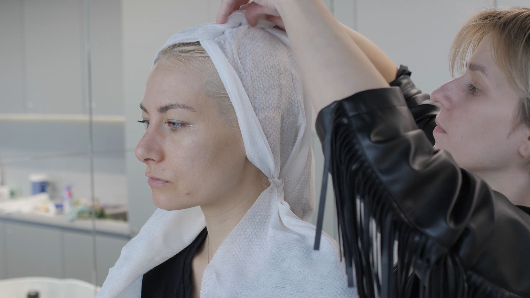 Ilinca așază prosopul alb pe capul clientei; mâneca tunicii are franjuri negri.
