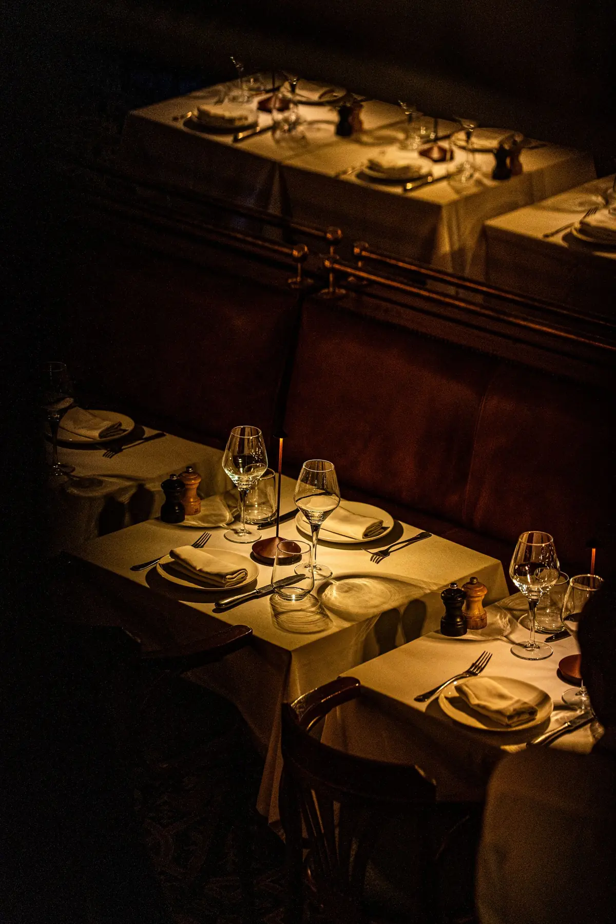 Sala seara: mese cu fețe de masă albe, pahare de vin și lumânări, banchete de piele maro de-a lungul peretelui.