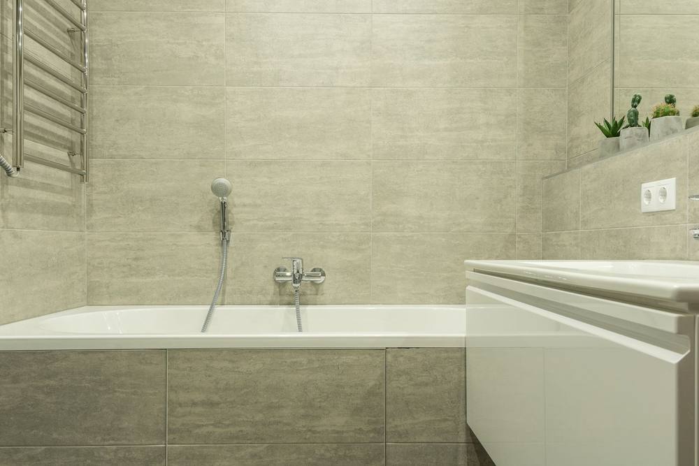 Cadă cu masca placată în plăci gri 30 × 60; rosturile cad pe muchia căzii, priza dublă stă într-o singură placă.