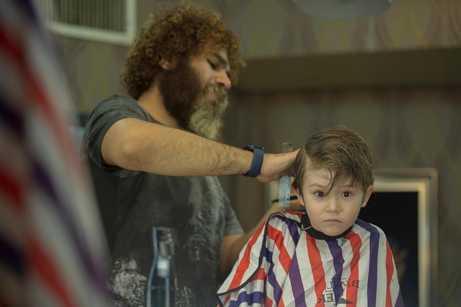 Arman tunde un băiat cu pelerina cu dungi roșii și violet, care stă nemișcat și se uită înainte.