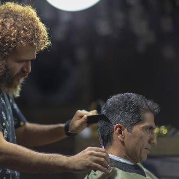 Arman, în cămașă cu desene, tunde ceafa unui domn grizonat.