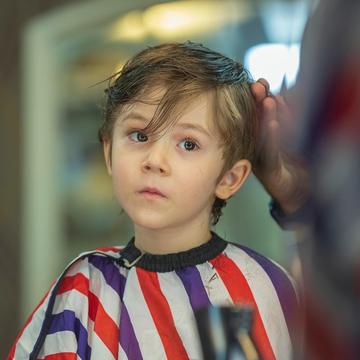 Un băiat de vreo șase ani, cu pelerina cu dungi roșii și violet, se uită serios în oglindă.