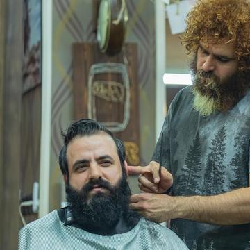 Un client cu barbă neagră mare zâmbește; Arman îi conturează barba lângă ureche.