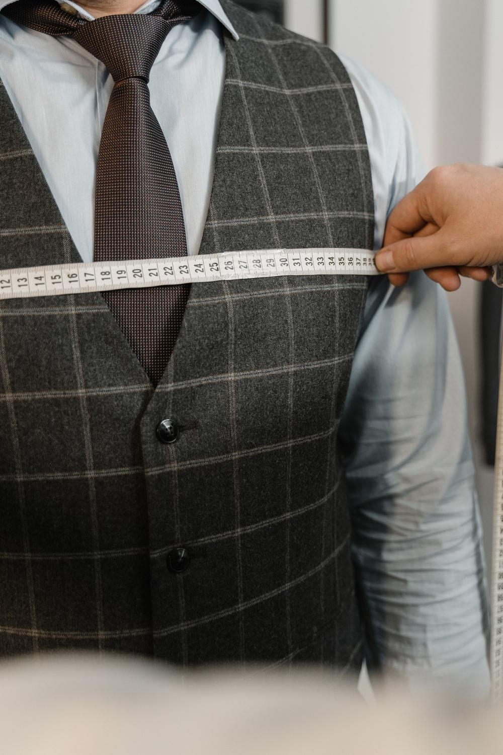 Centimetrul întins orizontal peste pieptul unei veste gri în carouri, sub nodul cravatei.